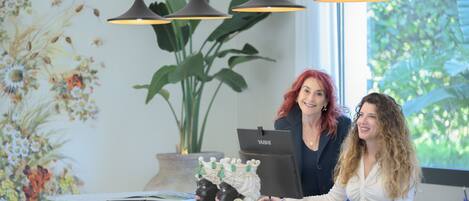 A reception desk with a laptop, a decorative vase, and a potted plant.