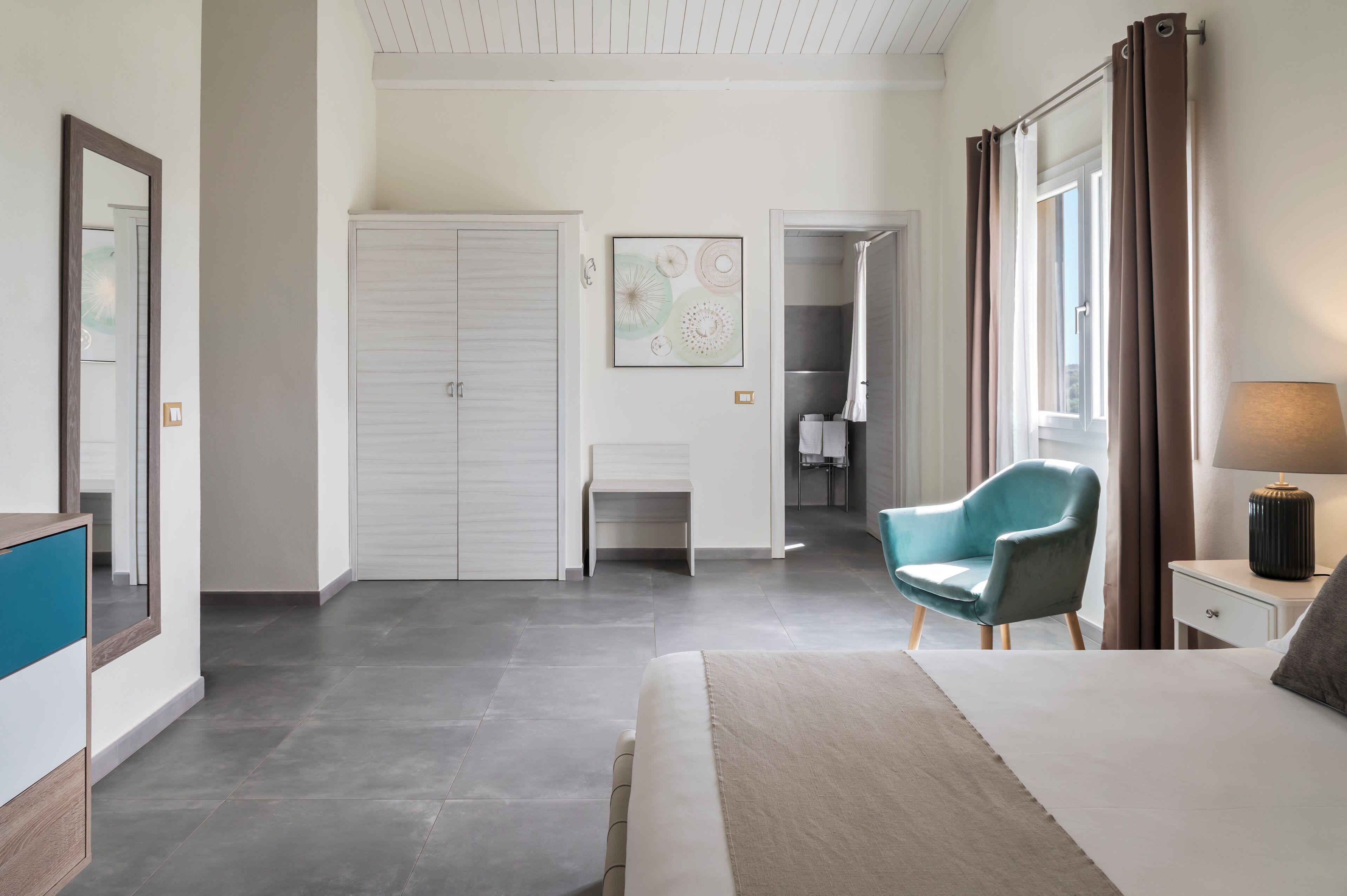 A modern hotel room with a large bed, a desk, a chair, and a bathroom visible through an open door.