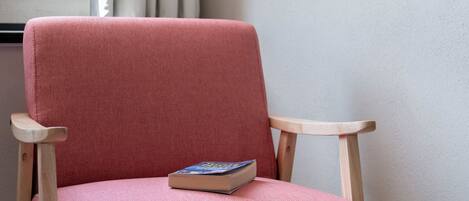 A red upholstered chair with a book on it, positioned near a window with curtains.
