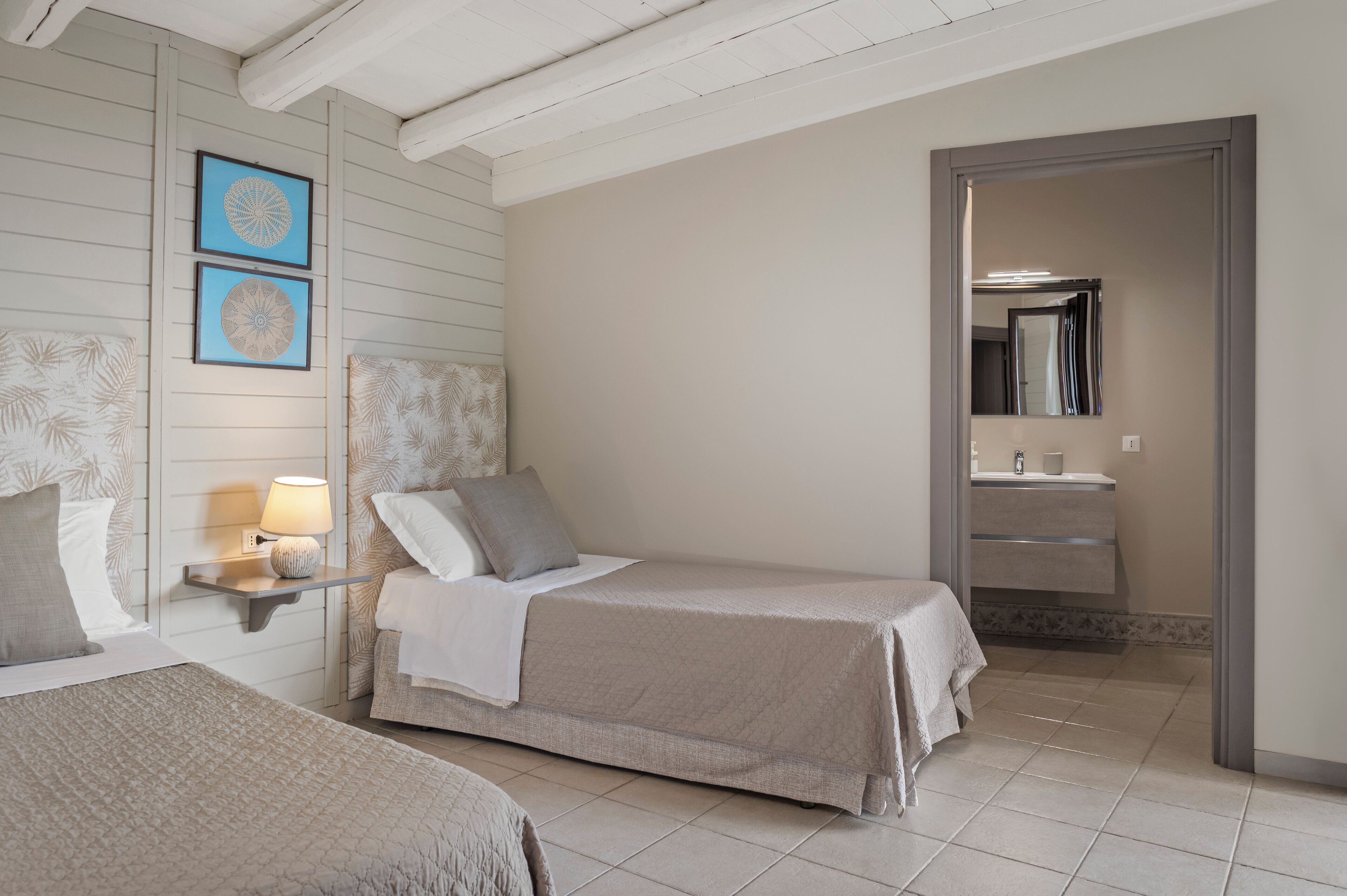 Een slaapkamer met twee bedden, een nachtkastje met een lamp, en een zichtbare badkamer door een open deur.