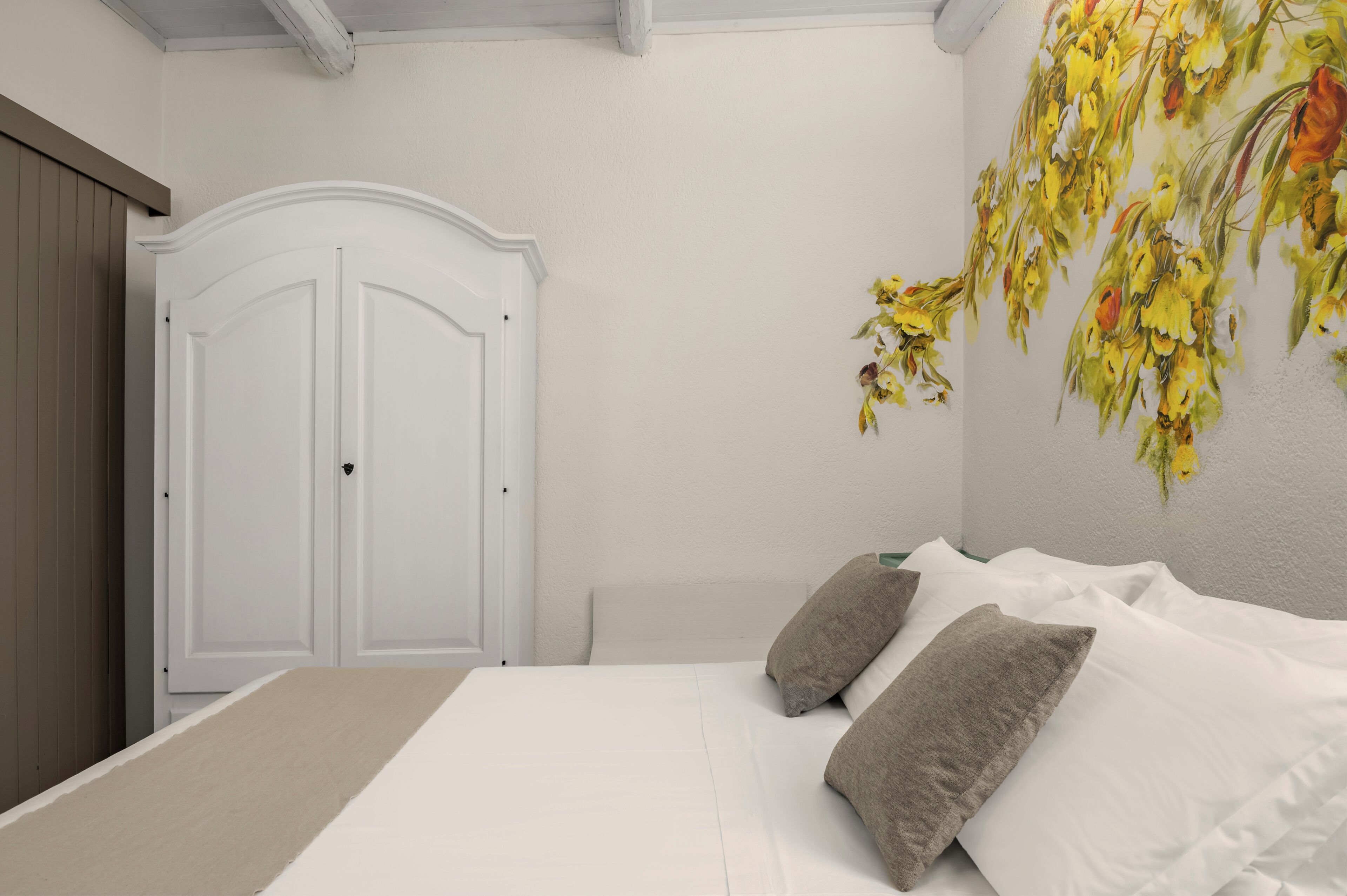 A bedroom with a bed, two pillows, a white wardrobe, and a floral wall decoration.