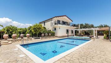 A swimming pool with a tiled deck, a two-story building with a balcony, and potted plants around the pool area.