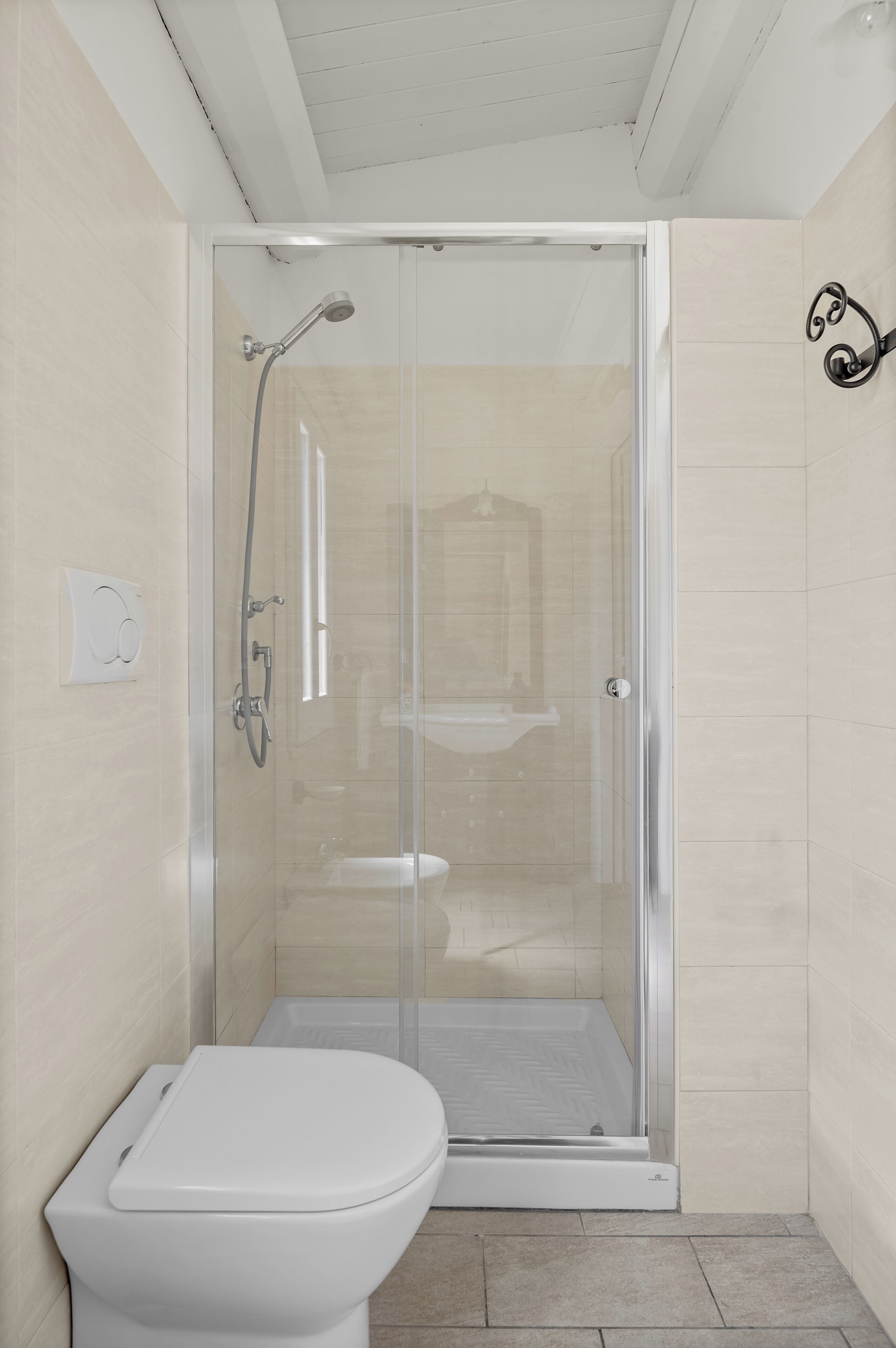 A small, enclosed shower area with a glass door, a toilet, and a sink visible through the door.