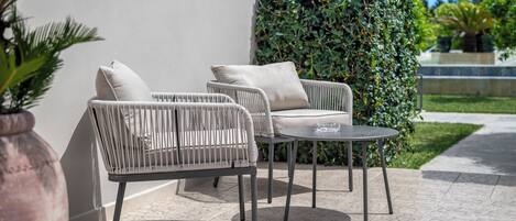 Un espace extérieur aménagé avec des chaises en osier et une table ronde, entouré d’une haie basse et d’un pot de fleurs.