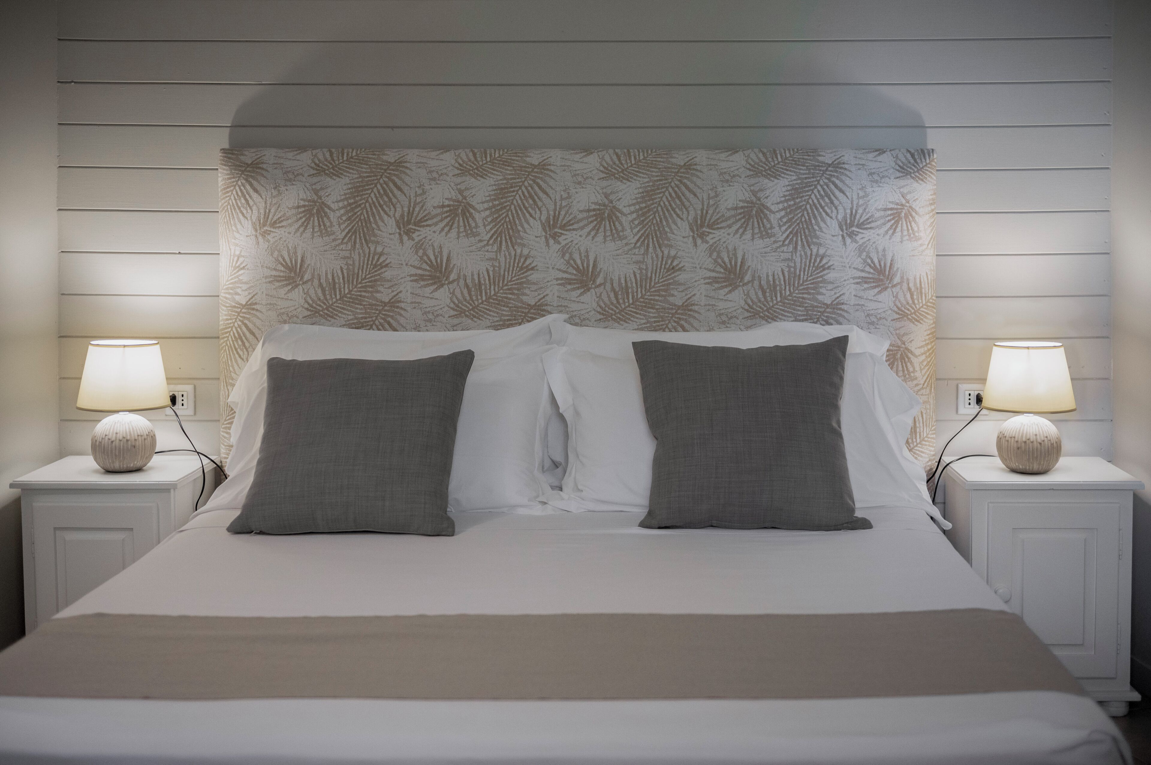 A neatly made bed with a white and gray color scheme, flanked by two bedside tables with lamps.