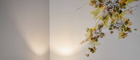 A neatly made bed with a grey pillow, a bedside lamp, and a wall-mounted floral decoration.