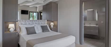 A bedroom with a bed, bedside lamps, a wardrobe, and a bathroom with a sink and mirror.