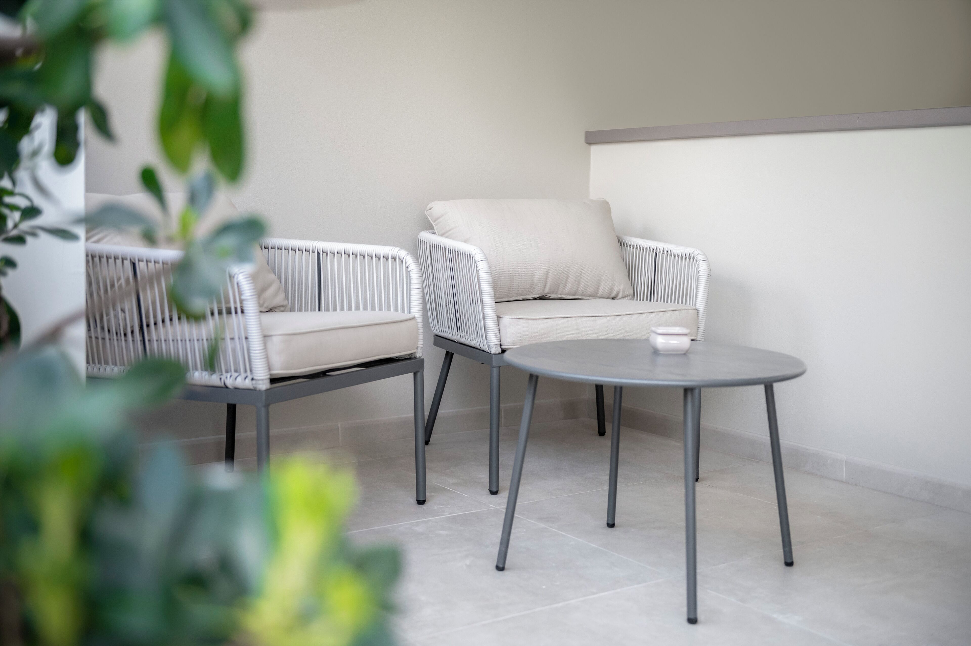 A modern outdoor seating area with two white wicker chairs and a round table, featuring a minimalist design and a neutral color palette.