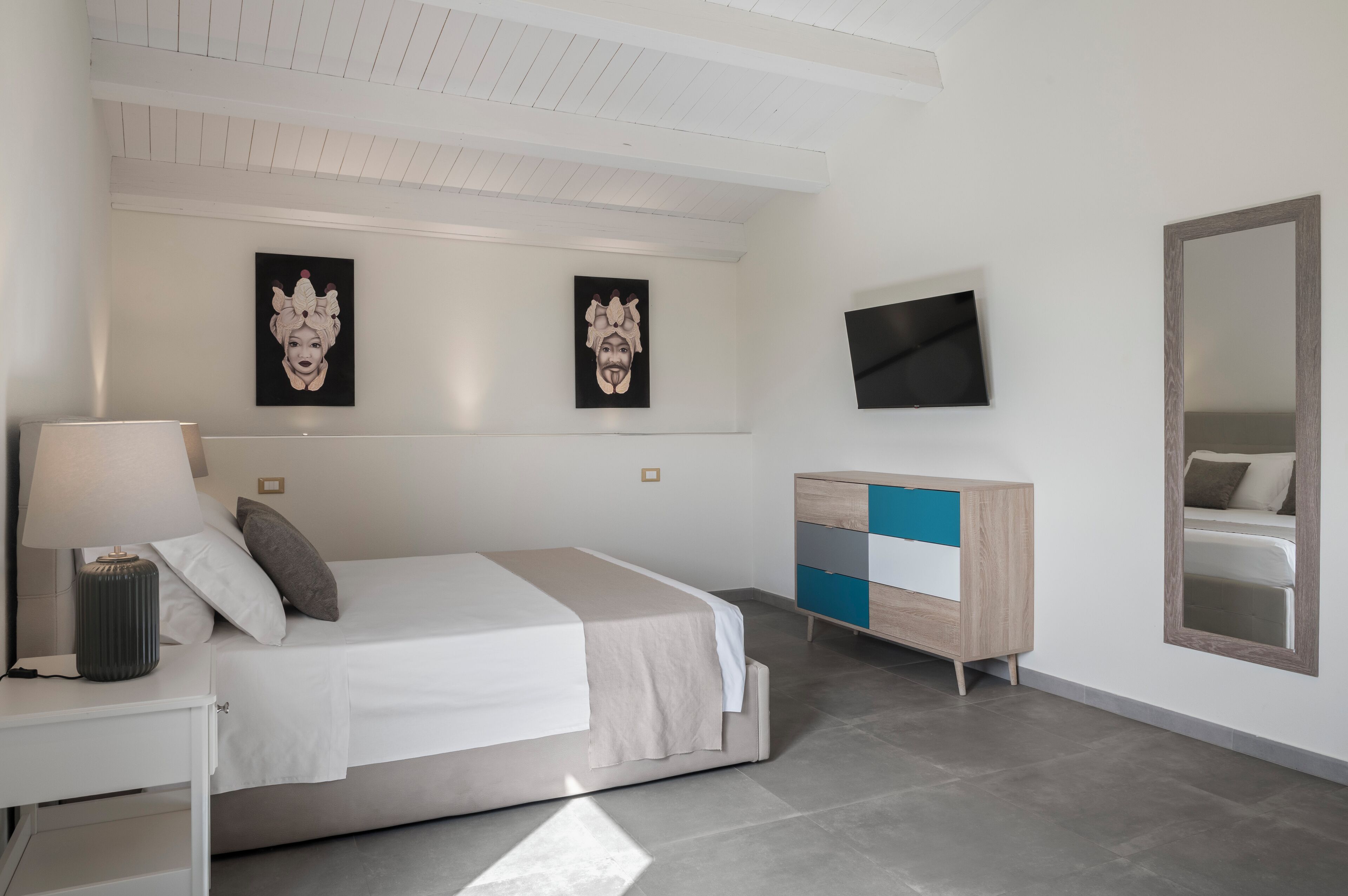 A modern bedroom with a bed, bedside table, TV, and artwork on the wall.