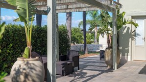 Un área de patio al aire libre con una pérgola, asientos y grandes macetas con plantas.
