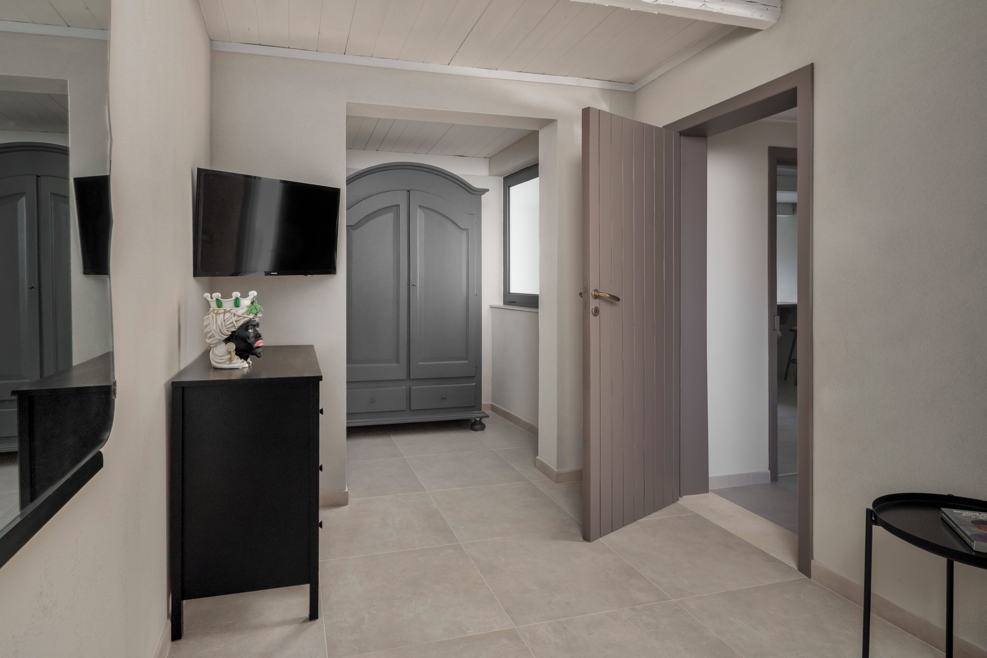 A hallway with a black console table, a gray wardrobe, and a door leading to another room.