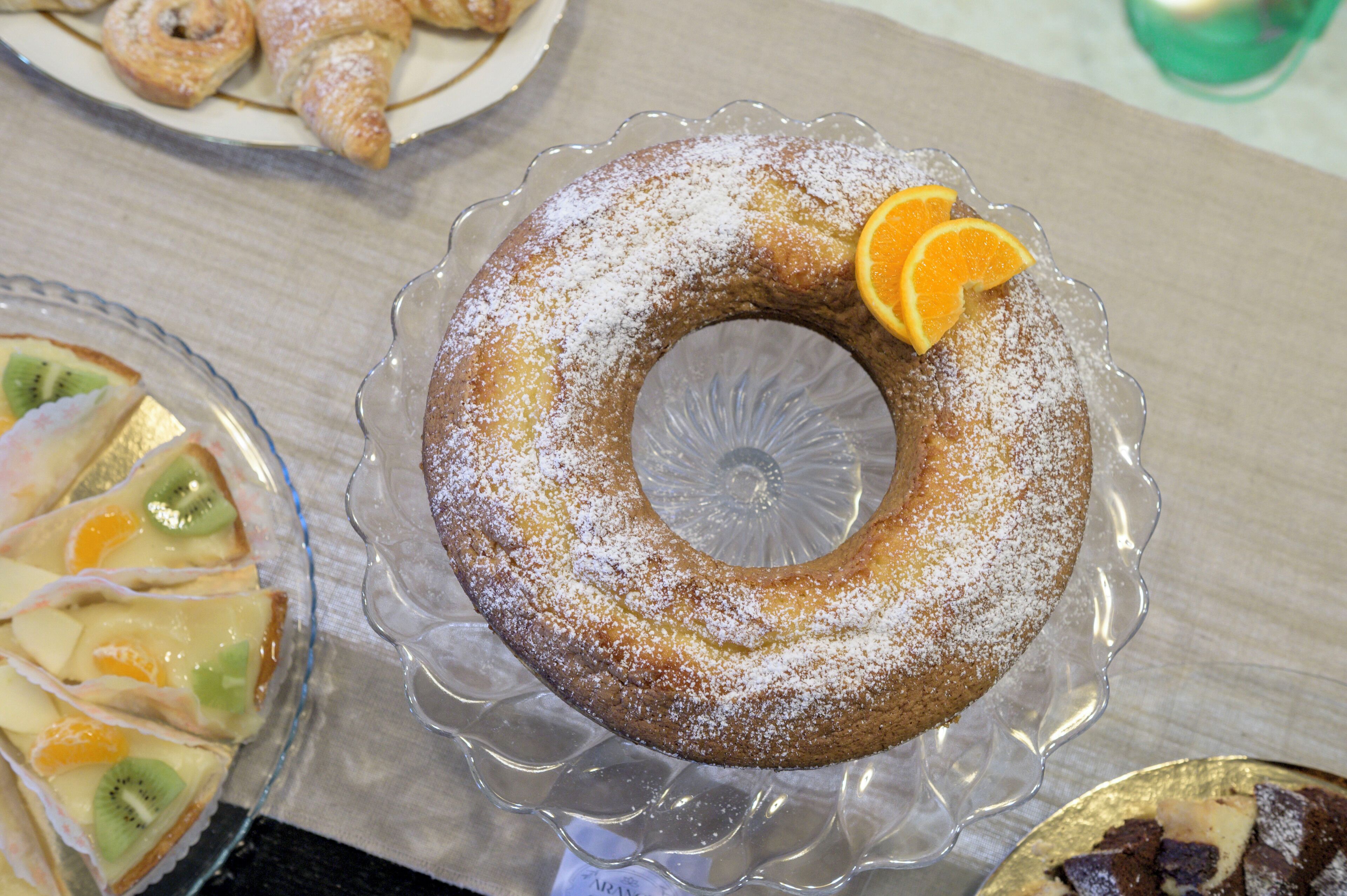 A bundt cake with powdered sugar and an orange slice on a glass plate.