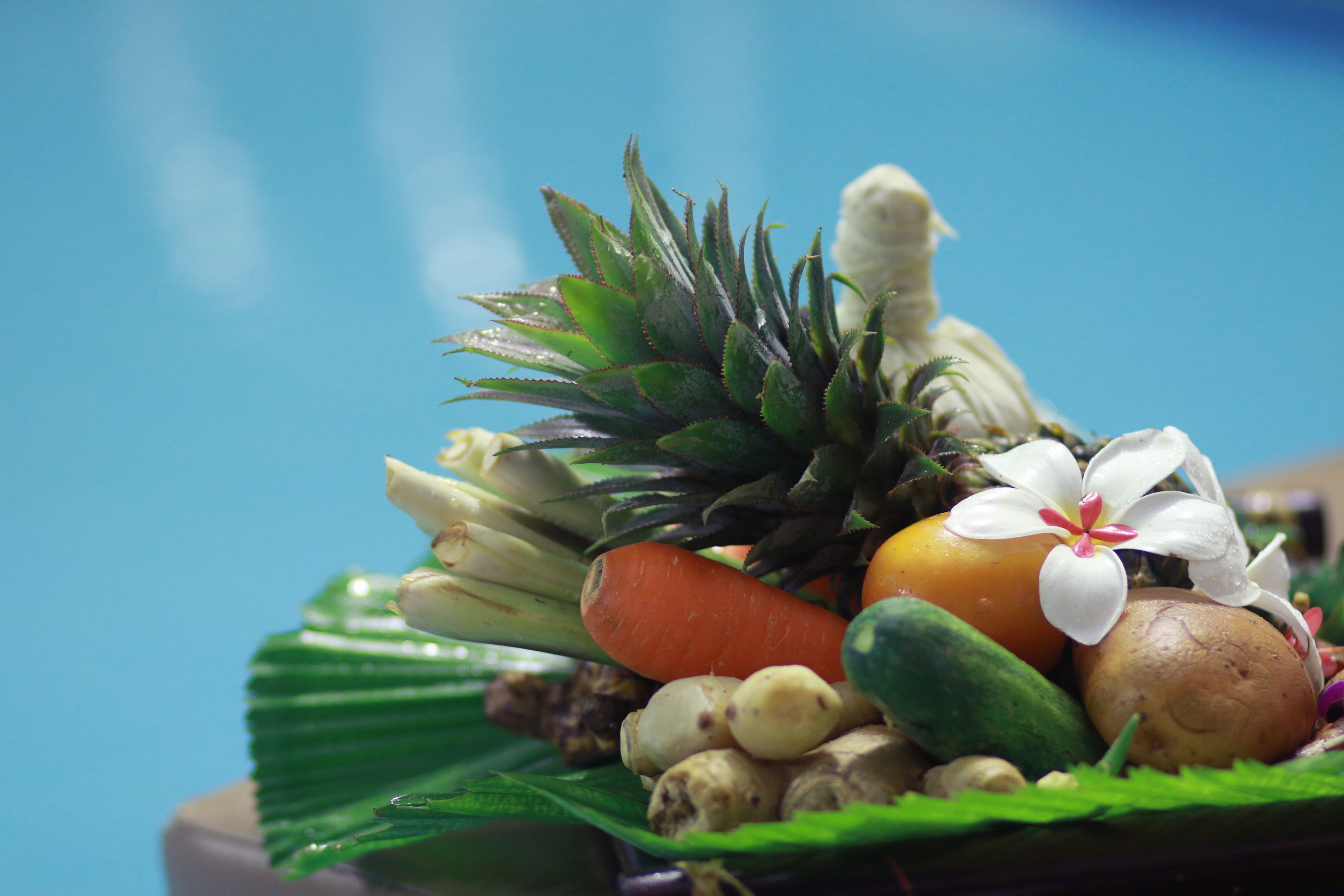 A variety of fresh fruits and vegetables including pineapple, carrots, and potatoes, arranged on a green leaf.
