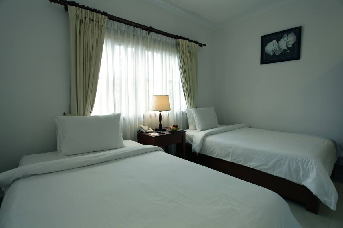 Habitación de hotel con dos camas individuales, una mesita de noche con lámpara, teléfono y una bandeja de frutas.