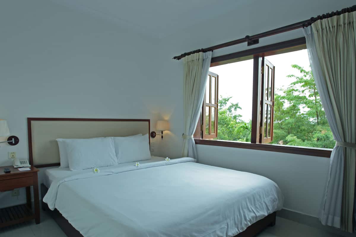 Una habitación de hotel con una cama individual, una mesita de noche con lámpara y una ventana con cortinas.
