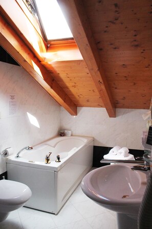 Un baño con tragaluz, bañera, lavamanos e inodoro.