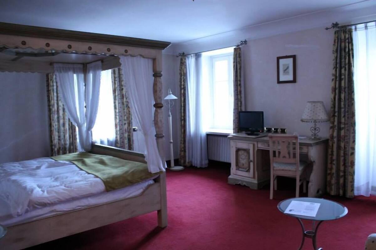 A room with a four-poster bed, a desk with a computer, a chair, and a small table.