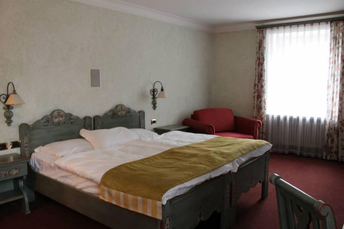 A bedroom with a bed, a nightstand, a chair, and a window with curtains.