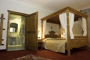 Una cama con dosel adornada con cortinas blancas, una puerta de madera y un baño con lavabo y espejo.
