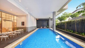 A modern indoor swimming pool with clear blue water, surrounded by lounge chairs and a glass wall.