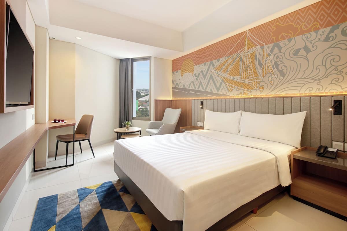 Een hotelkamer met een groot bed, een bureau met stoel, een televisie en een behang met patroon.