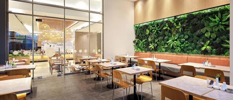 Un restaurante moderno con paredes de vidrio, mesas de madera y una pared verde con plantas.