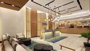 A modern hotel lobby with a reception desk, seating area, and a large mirror reflecting the space.