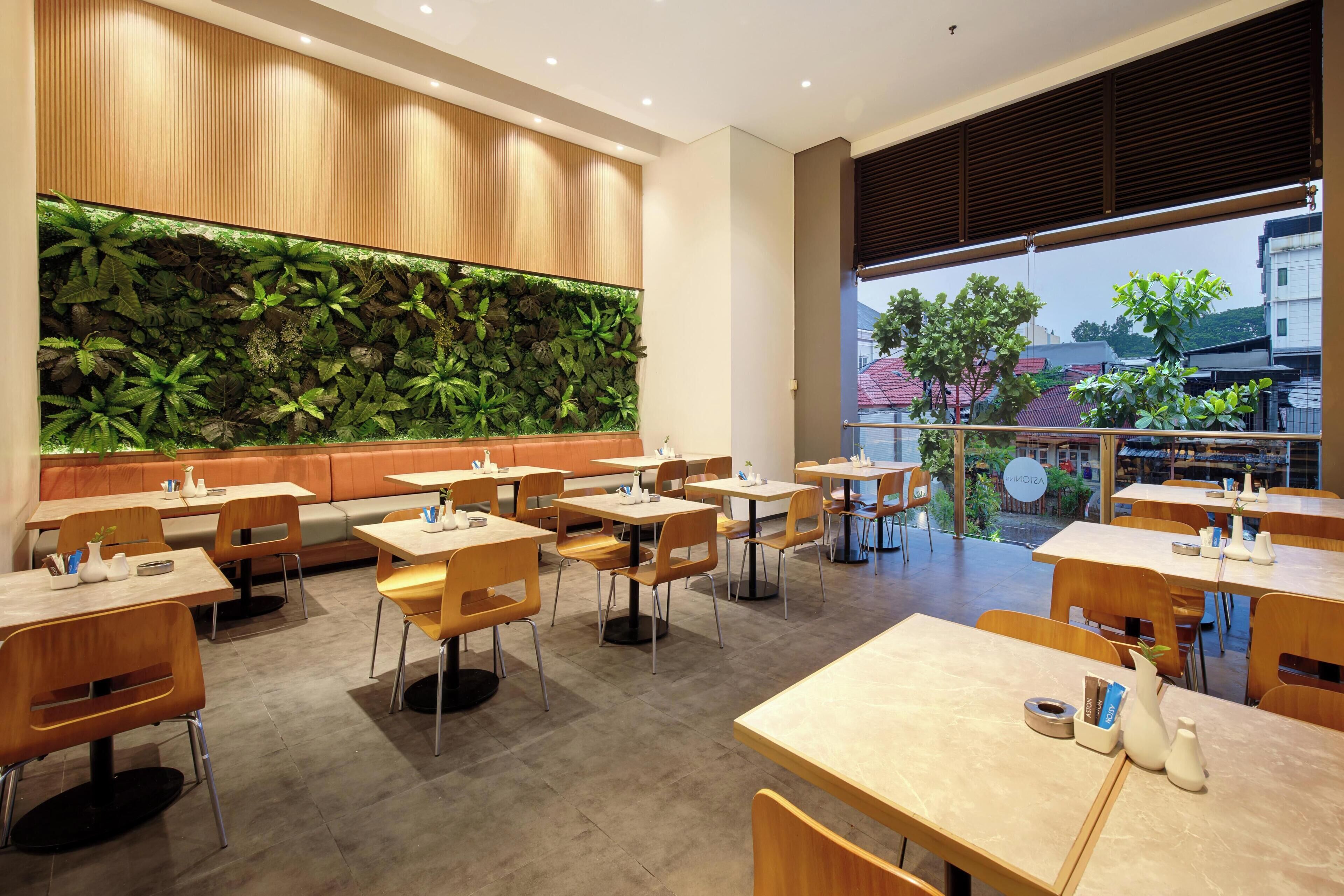 A modern restaurant with a green wall, wooden furniture, and a view of the city.