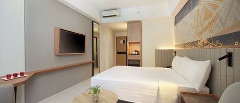 A modern hotel room with a large bed, a TV mounted on the wall, a small table with a plant, and a seating area with a chair.