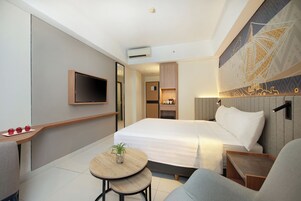 Una habitación de hotel moderna con una cama grande, un televisor montado en la pared, una mesita con una planta y una zona de estar con un sillón.