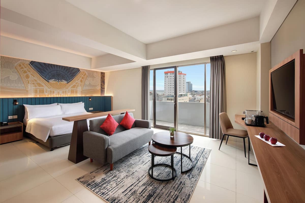 Een moderne hotelkamer met een bed, een bank, een eettafel en een televisie.