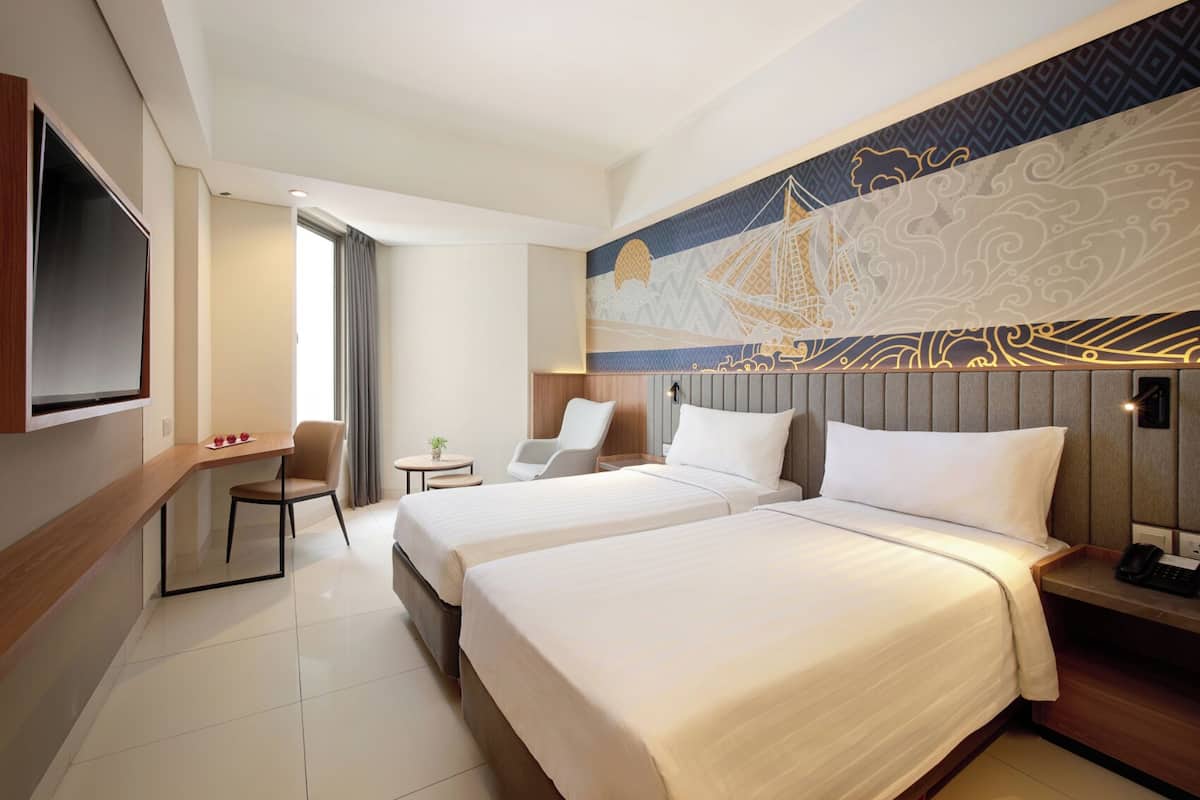Een hotelkamer met twee bedden, een bureau, een stoel, een televisie en een decoratief muurschildering.