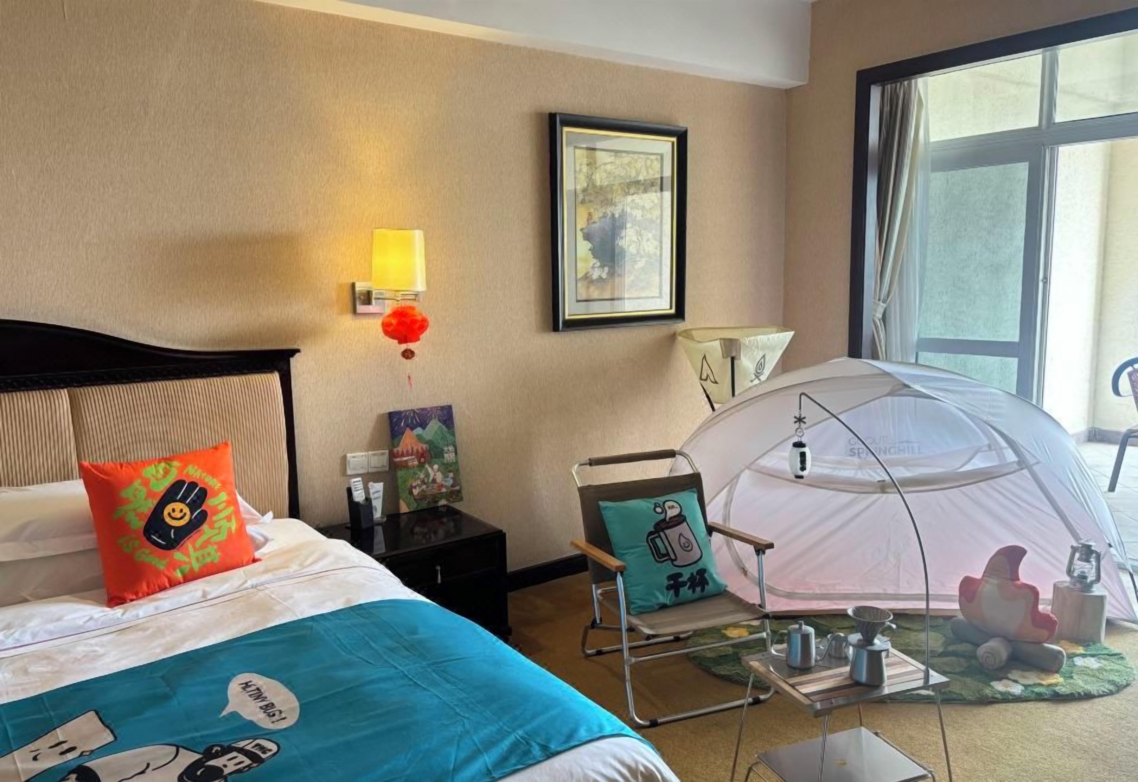 Una habitación de hotel con una cama, una tienda de campaña, una silla y una lámpara.
