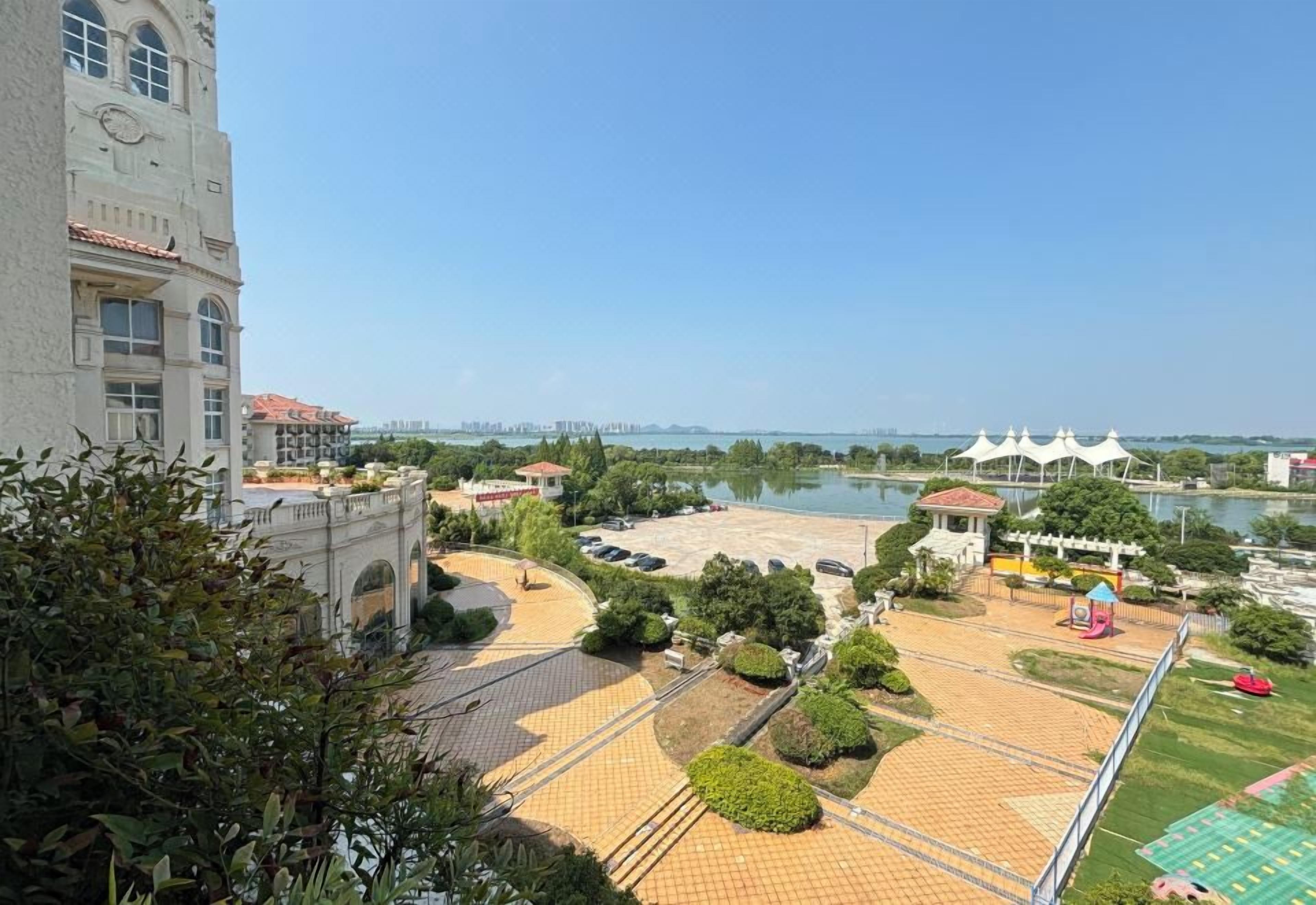 A park with a paved area, a water body, and a building with a clock tower.