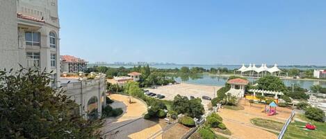 A park with a paved area, a water body, and a building with a clock tower.
