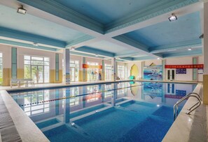 An indoor swimming pool with clear lanes, a tiled floor, and a ceiling with blue beams.