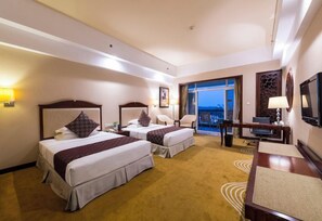 Quarto de hotel com duas camas, uma escrivaninha, uma cadeira, uma televisão e vista para o exterior.