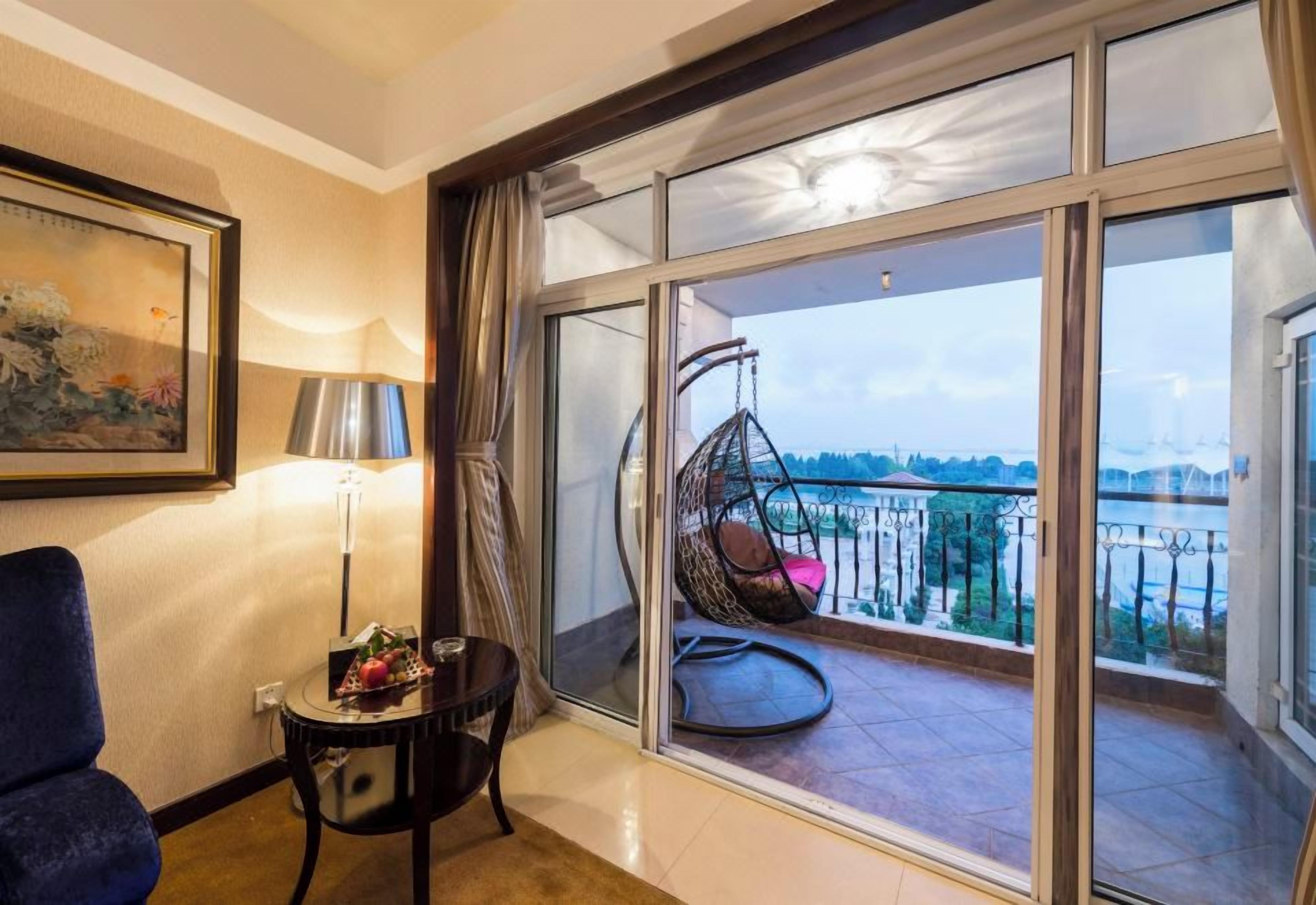 A room with a balcony, a hanging chair, a table with a lamp, and a framed picture on the wall.