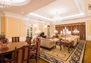 A spacious living room with a dining area, ornate chandeliers, and a patterned carpet.
