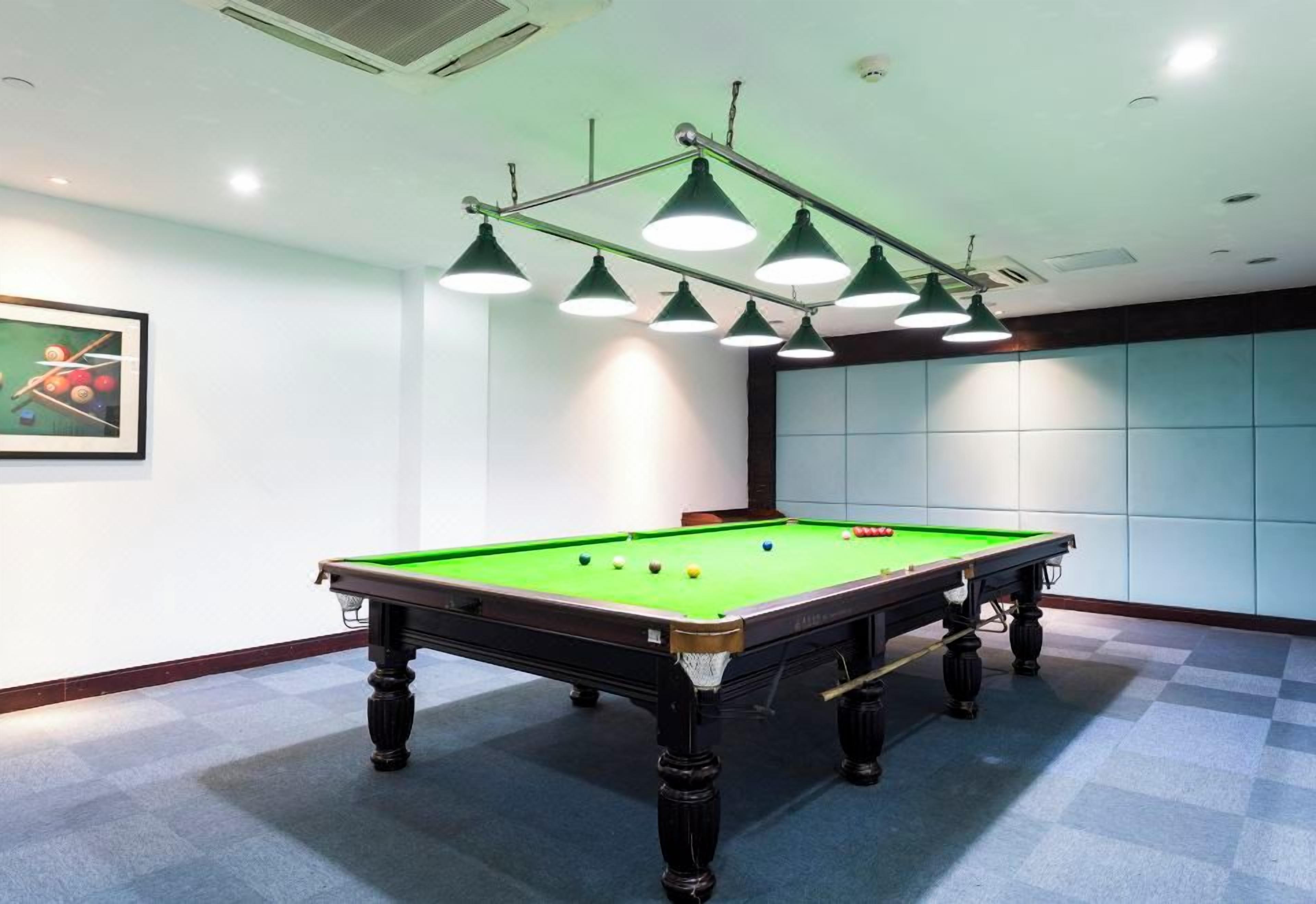 A pool table with a green felt surface, surrounded by a checkered floor, and overhead lighting fixtures.