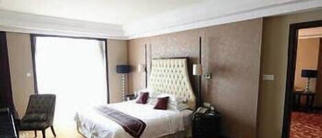 A hotel room with a bed, a chair, a desk, a lamp, and a door.