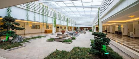 A spacious indoor courtyard with a glass ceiling, potted plants, and seating areas.