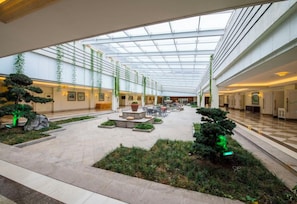 Un patio interior amplio con techo de vidrio, plantas en macetas y zonas de descanso.