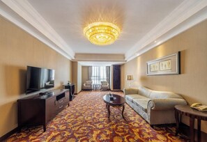 A hotel room with a large chandelier, a television, a sofa, a coffee table, and a patterned carpet. - Country Garden Phoenix Hotel (Wuhu)