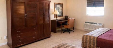 Une chambre avec une grande armoire en bois, un bureau avec une chaise, un lit avec une couette et une fenêtre avec un rideau.