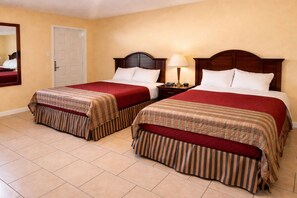 A hotel room with two beds, each with a wooden headboard, a nightstand, a lamp, and a door. - Alvin Extended Stay (Alvin)