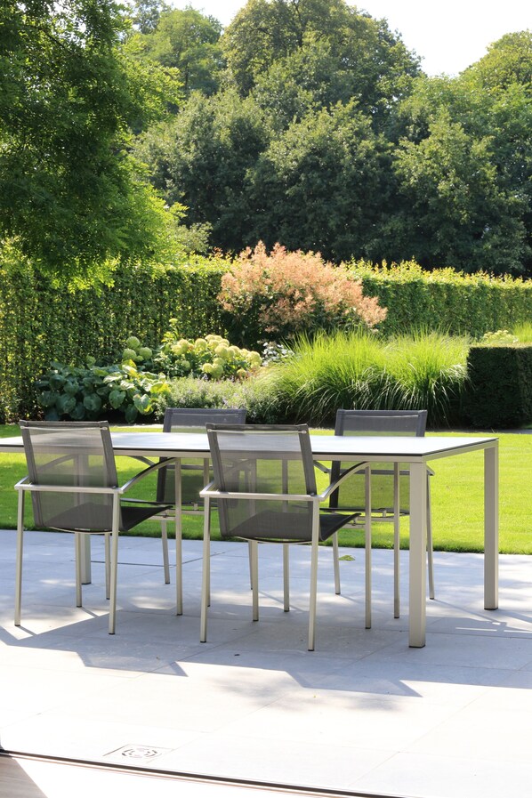 An outdoor patio with a table and chairs, surrounded by lush greenery and a hedge. - B&B Antares (Bruges)