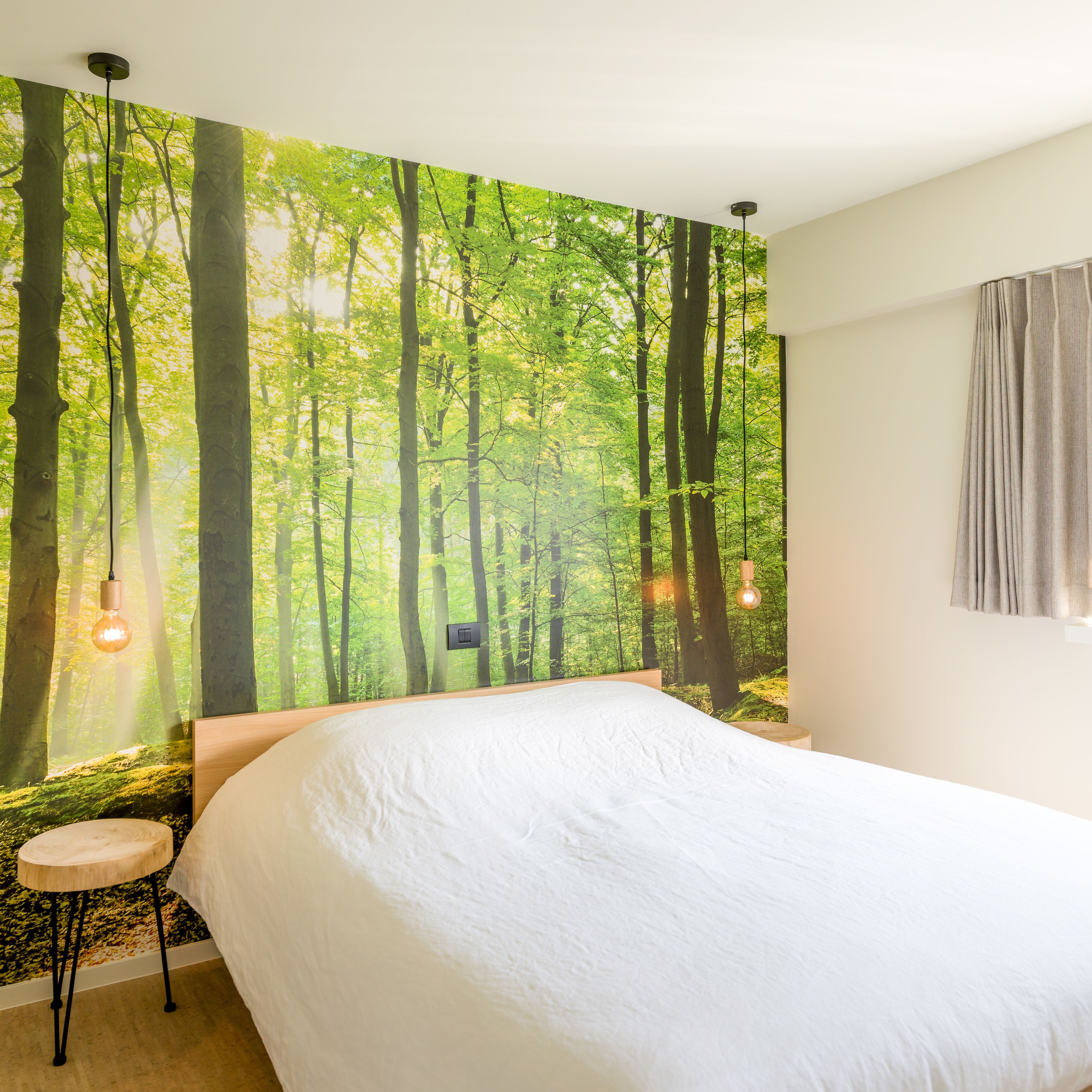 A bedroom with a large bed, a small round table, and a forest-themed wall mural.