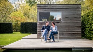 A couple sitting on a bench in a modern outdoor setting with a reflective water feature in front. - B&B Antares (Bruges)