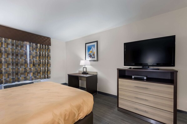 Una habitación de hotel con cama, televisión, escritorio con lámpara y cómoda.